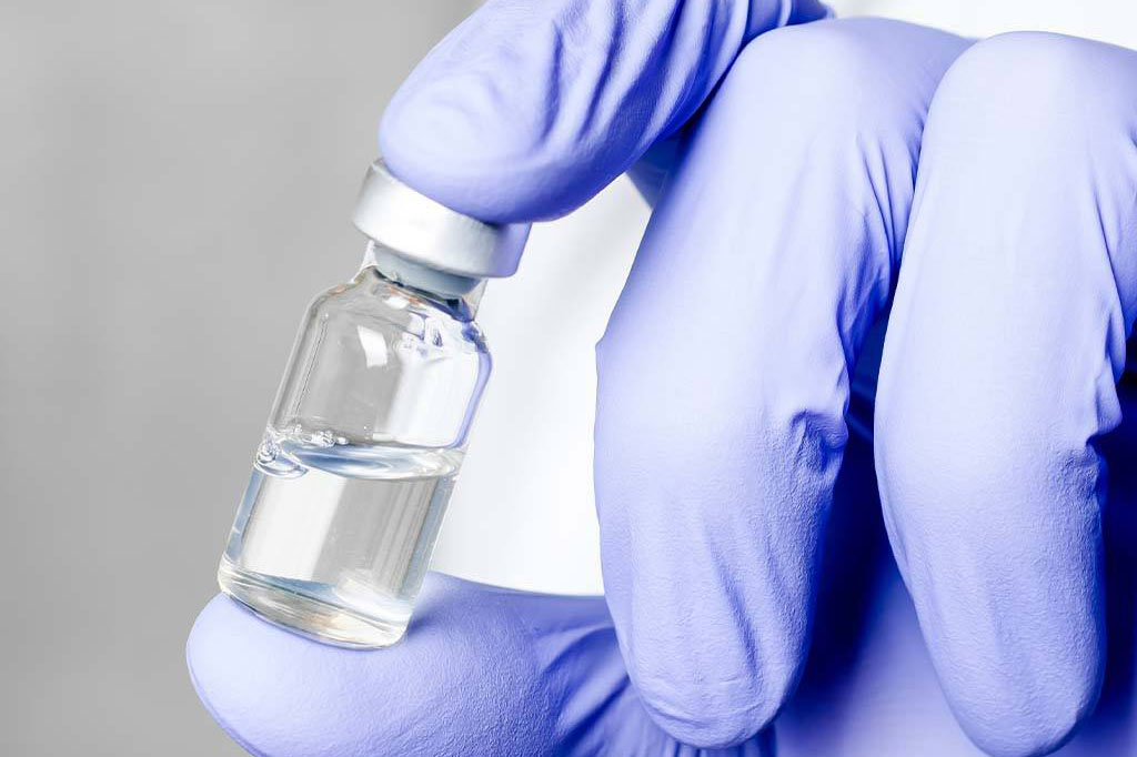 A gloved hand holds a vial of medication