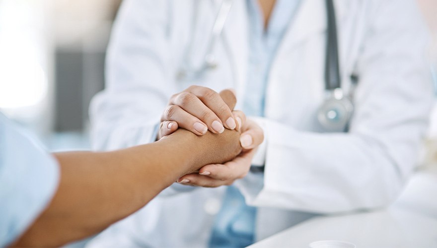 A doctor clasps the hand of a patient