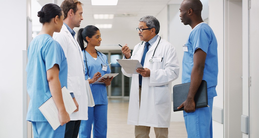 A team of doctors and nurses have a conversation in a hospital hallway