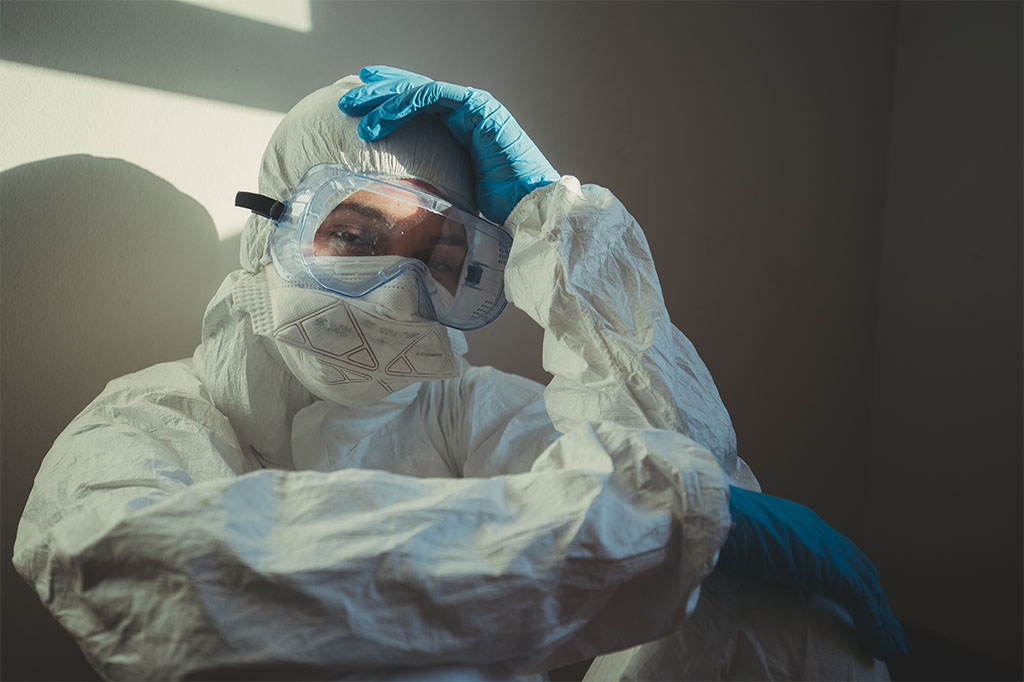 A medical professional in PPE rests in a hospital hallway