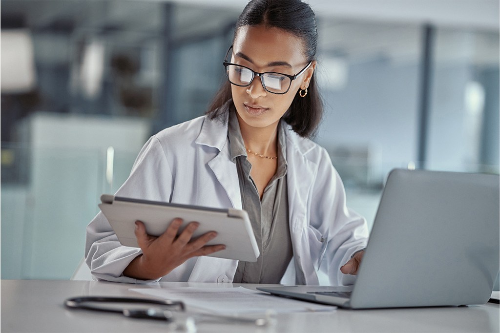 A doctor compares information on a tablet with a laptop computer