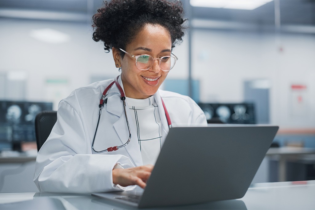 A doctor works at a desk with a laptop computer