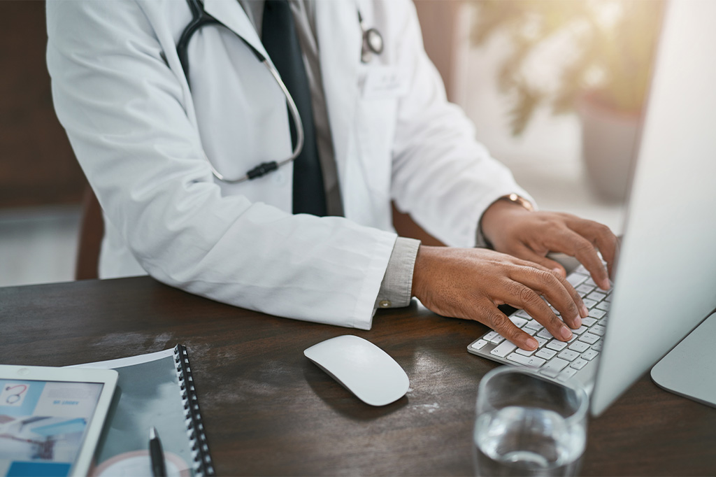 A doctor in white lab coat types on a keyboard