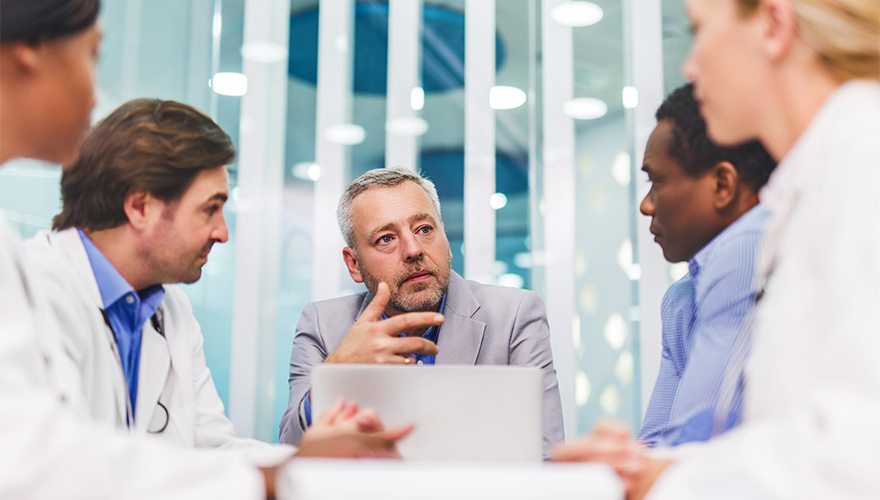 A consultant in professional wear speaks to a conference room full of doctors