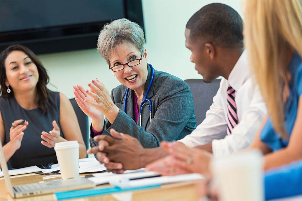 A group of administrators and doctors speak in a conference room