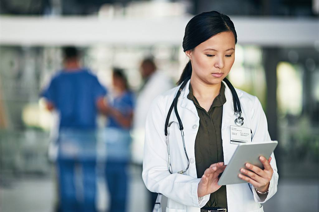 A doctor uses a tablet in a hospital hallway