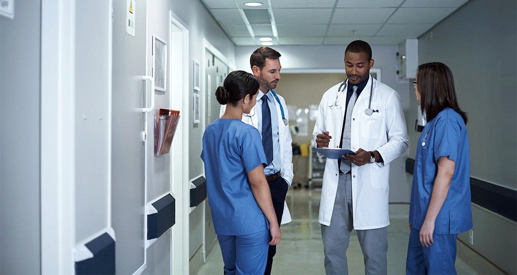 A team of doctors and nurses have a meeting in a hospital hallway