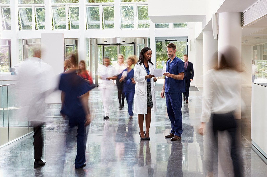 A doctor in white lab coat speaks with a nurse in scrubs